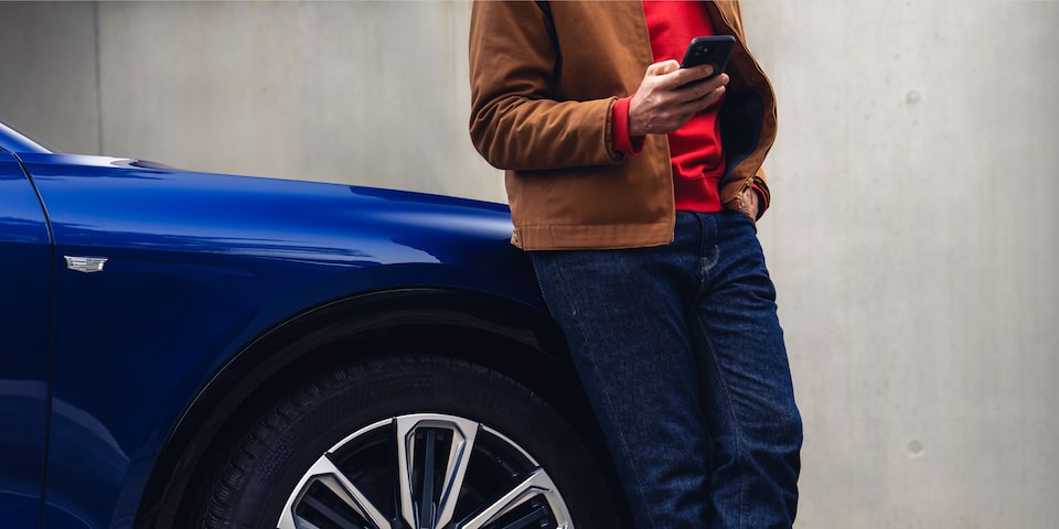 Eine Person steht neben einem Cadillac-Elektrofahrzeug und benutzt ein Smartphone.