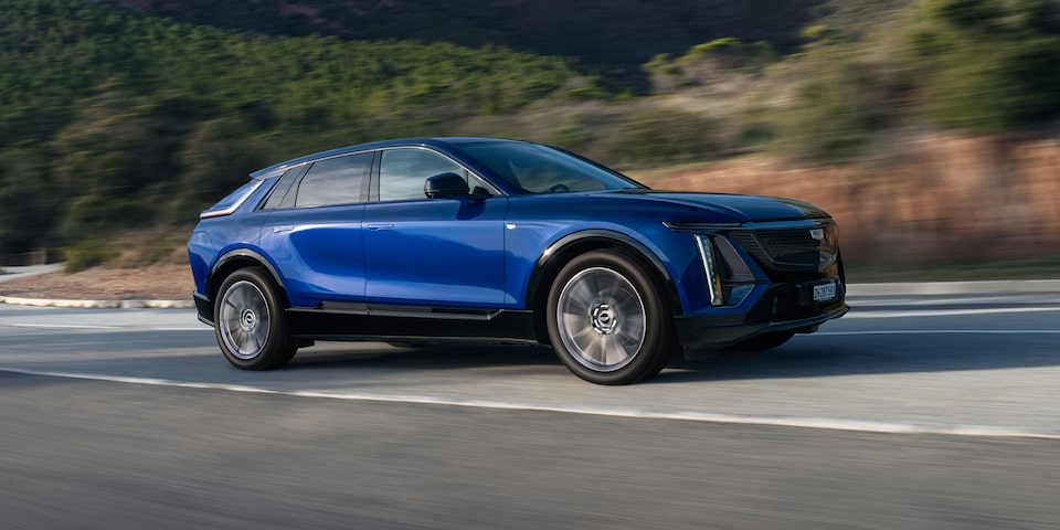 Ein Elektro-SUV Cadillac LYRIQ fährt auf einer asphaltierten Straße vor einer Landschaft im Hintergrund.