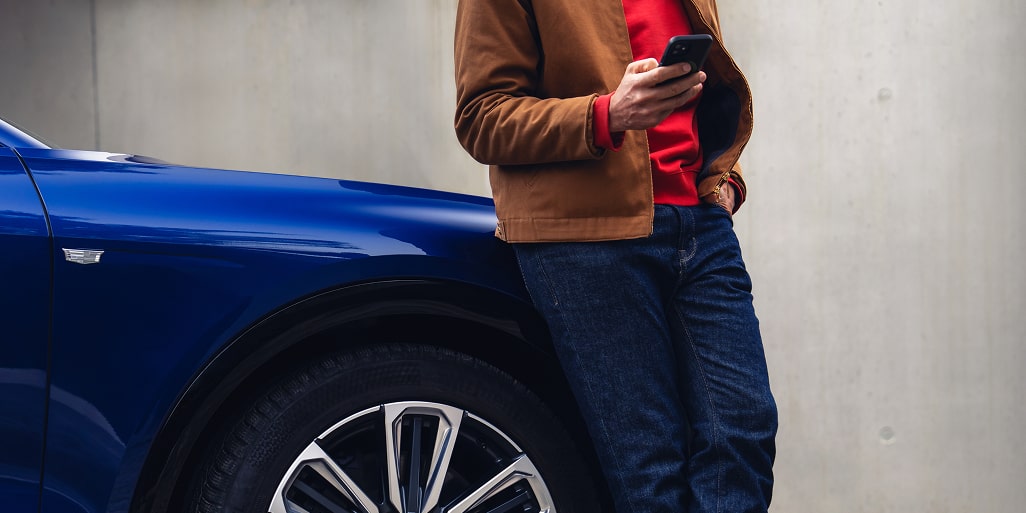 Person standing beside a Cadillac electric vehicle while using a smartphone. 