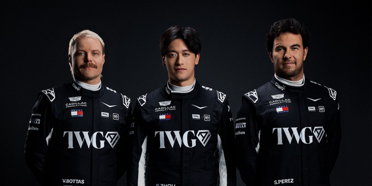 Three team members in black Cadillac racing suits stand shoulder to shoulder against a dark studio background.