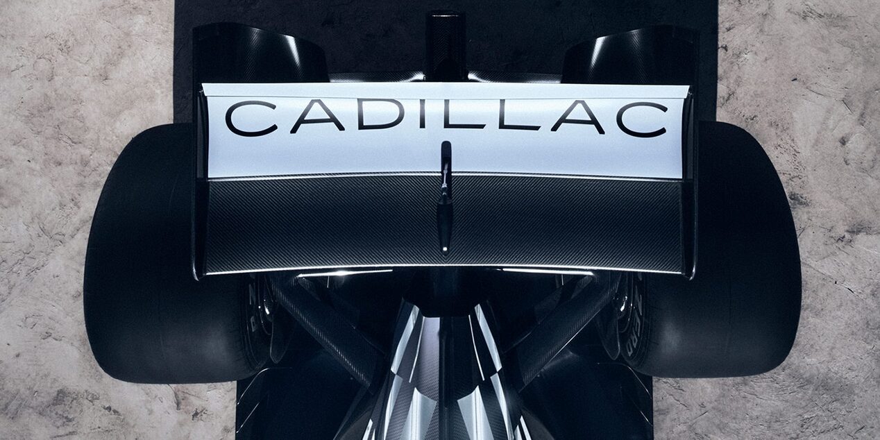 Aerial view of F1 car’s rear wing adorned with ‘CADILLAC’, and of rear wheels, with textured concrete beneath.