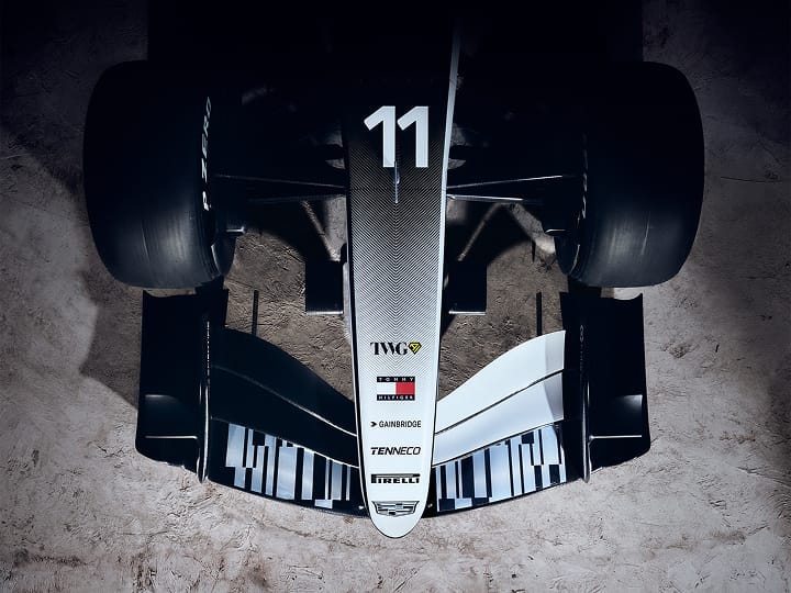 Aerial view of the Cadillac F1 car’s nose adorned with sponsors’ names, and front wing, with grey rocky surface beneath.