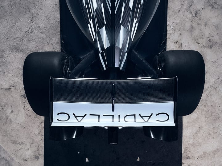 Aerial view of F1 car’s rear wing adorned with ‘CADILLAC’, and of rear wheels, with textured concrete beneath.