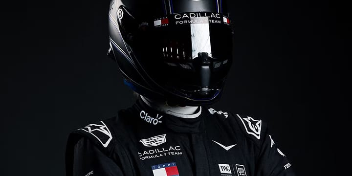 A Forumla 1 driver's head in glossy black Cadillac racing helmet against a dark studio background