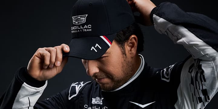 A team member wearing a black, Cadillac-branded cap adjusts the brim against a dark studio background.