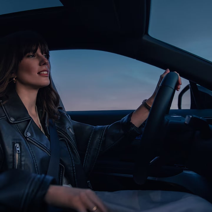 Femme conduisant un véhicule électrique d’occasion / certifié d’occasion Cadillac au crépuscule.