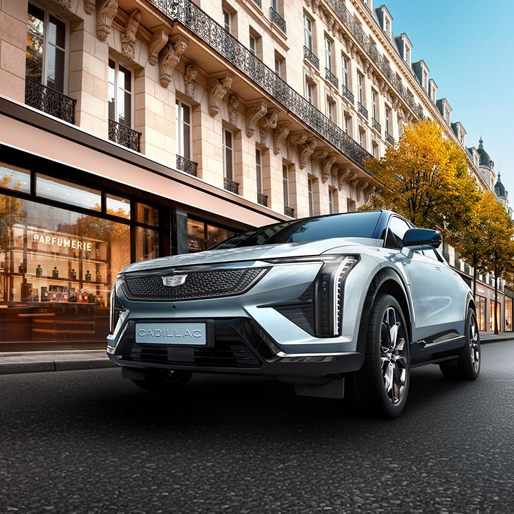 Cadillac OPTIQ Studio Edition, SUV électrique premium, longeant une parfumerie parisienne et révélant son design audacieux au cœur d'un environnement urbain européen