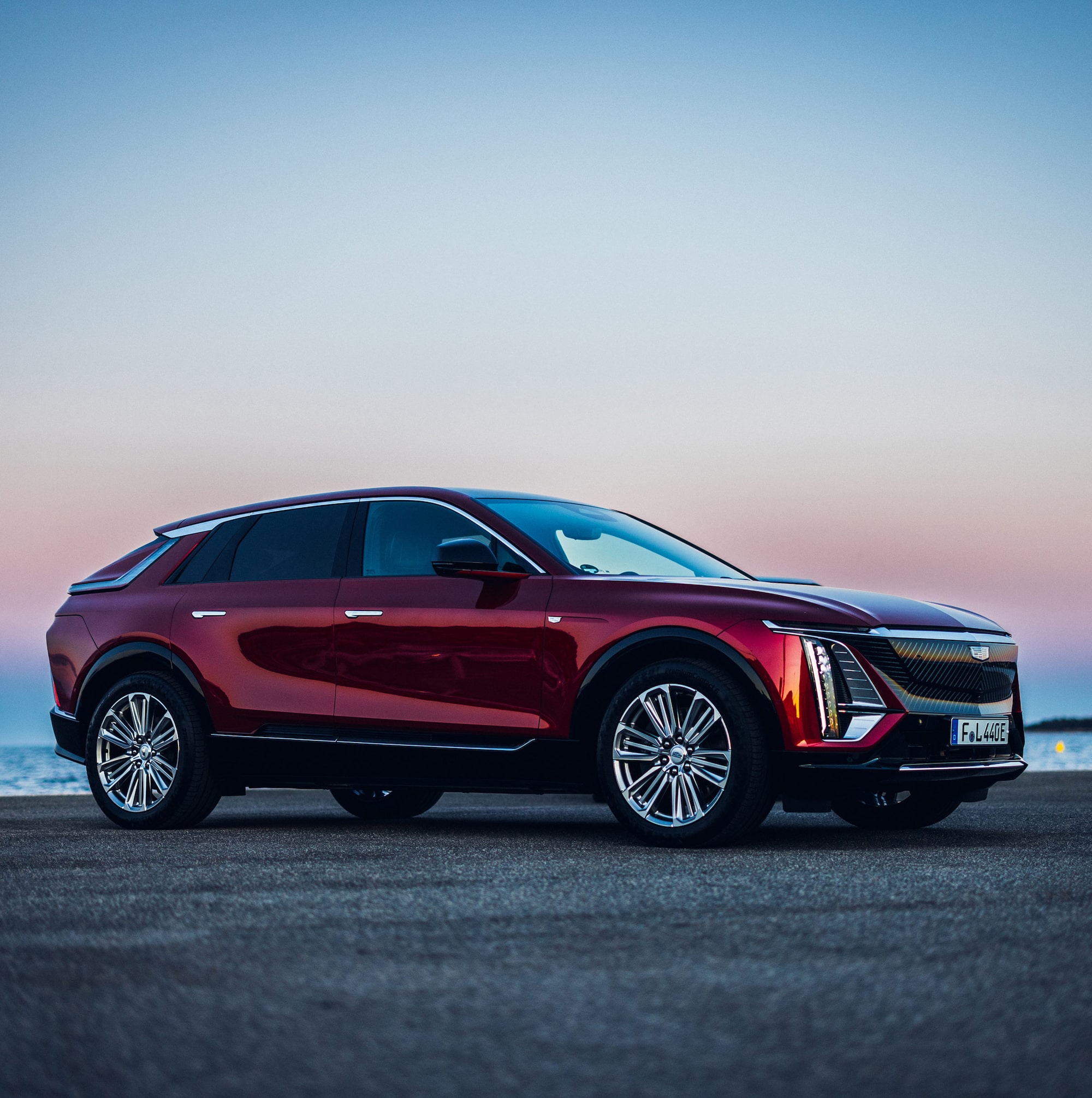 Cadillac LYRIQ electric SUV parked and charging in the driveway of a modern residential property.