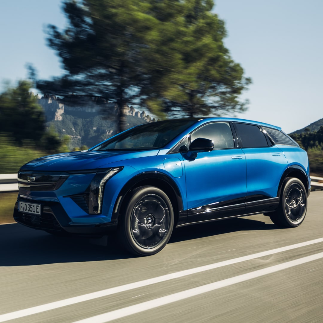 Three-quarter view of OPTIQ, in Coastal Blue Metallic, cruising a country highway.