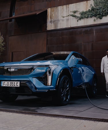 Cadillac LYRIQ electric SUV parked and charging in the driveway of a modern residential property.