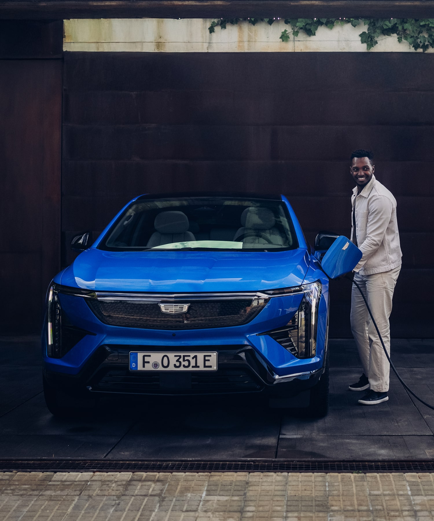 Homme branchant un SUV électrique Cadillac LYRIQ devant un immeuble résidentiel.