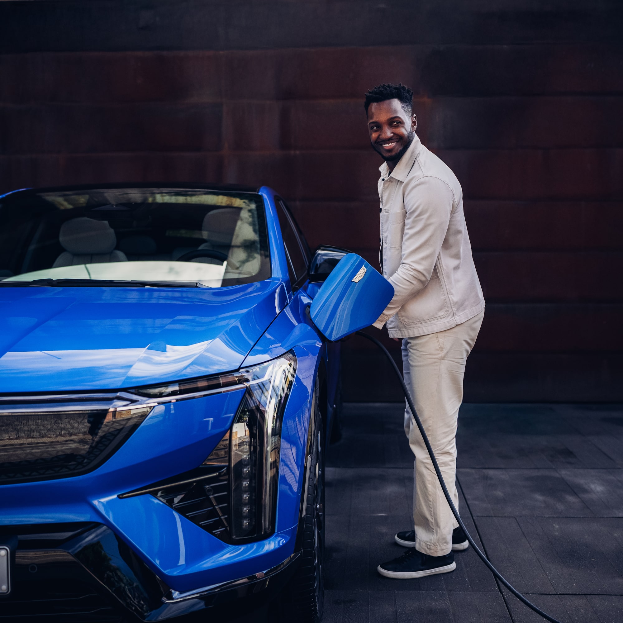 Homme branchant un SUV électrique Cadillac LYRIQ devant un immeuble résidentiel.